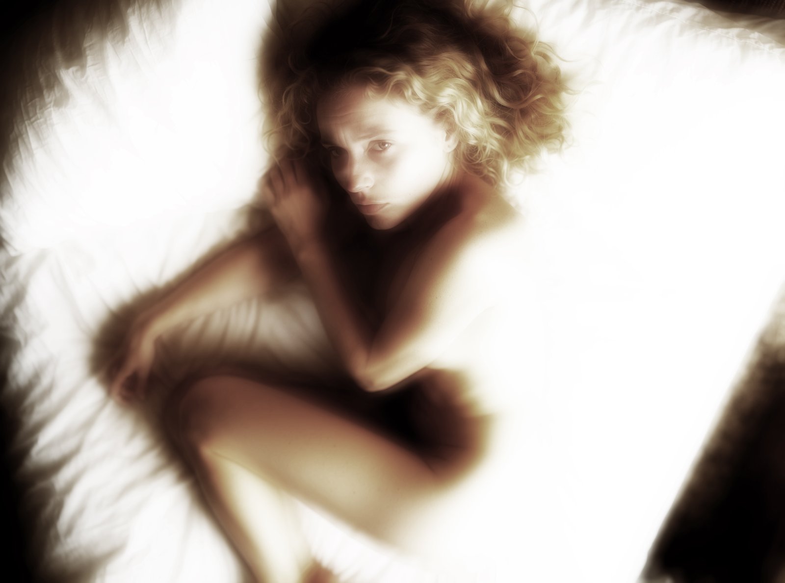 Soft-focus overhead portrait of Dina reclining on white bedding