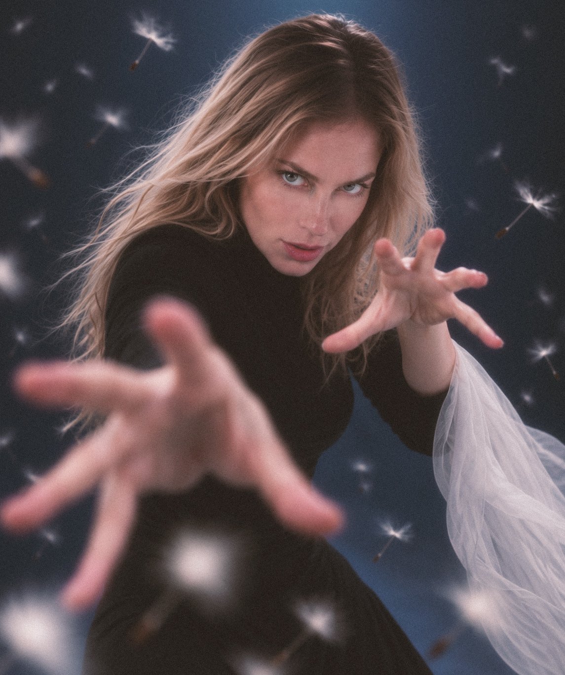 Lottie reaching toward the camera in a dark studio portrait with floating seeds