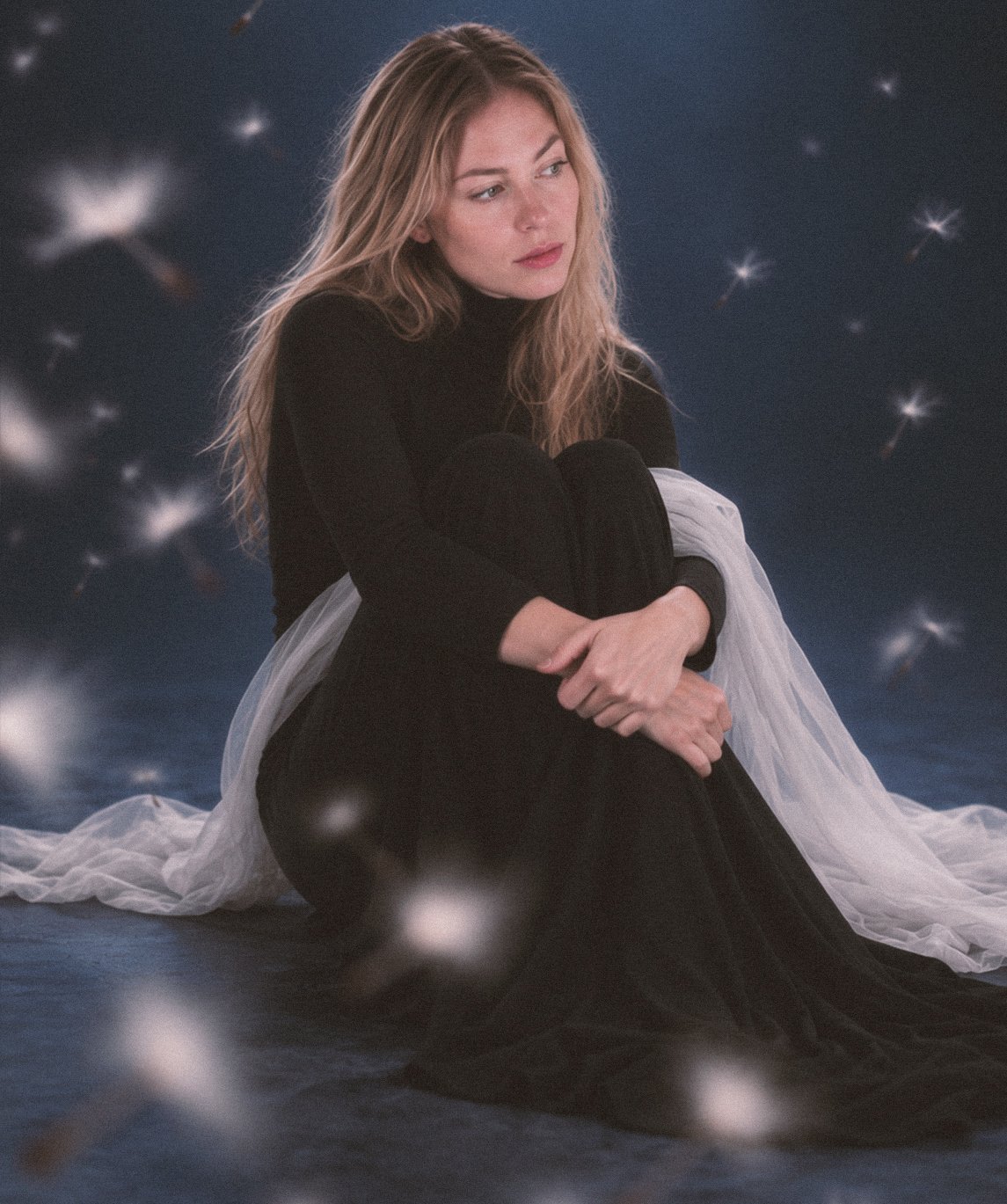 Lottie seated in a dark studio portrait with floating seeds