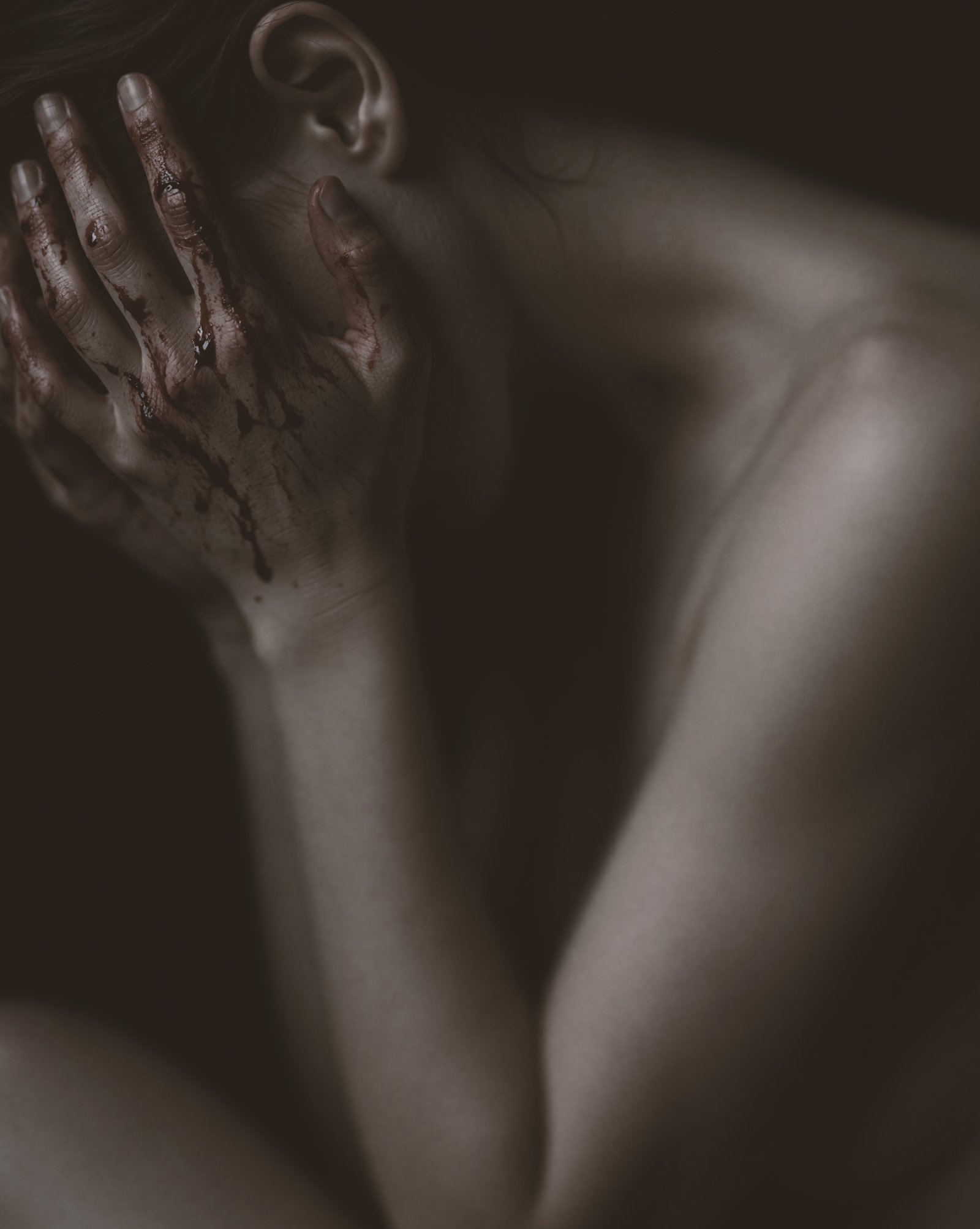 Low-key close portrait of Mette touching her neck with red-stained hands