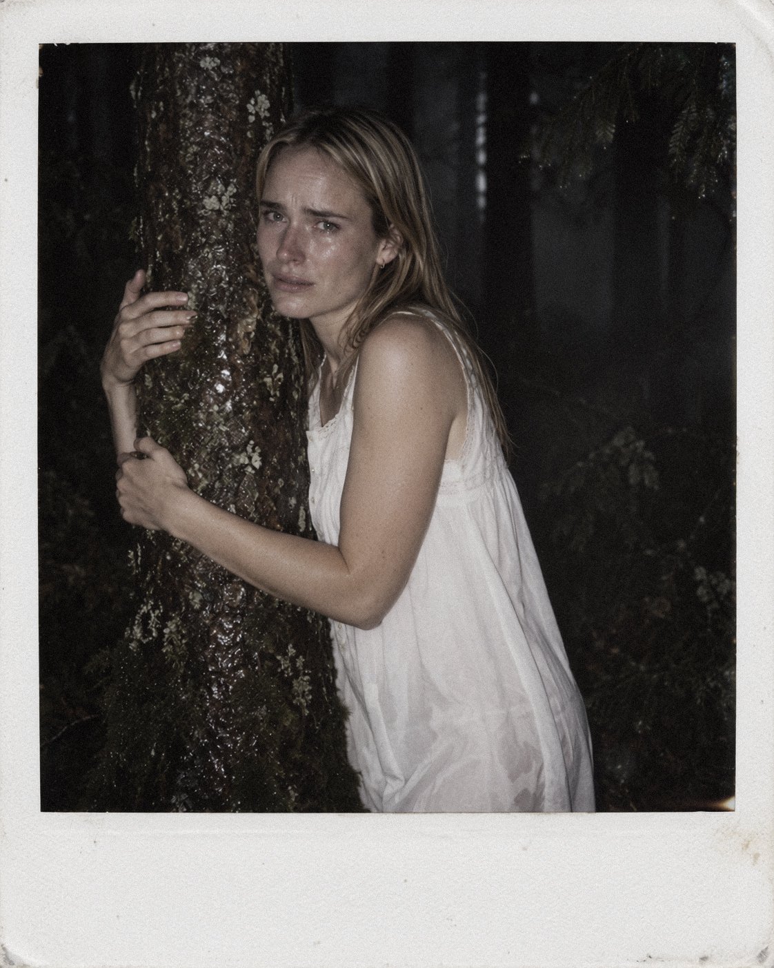 Nightmare series portrait of a distressed woman holding a tree in a dark forest